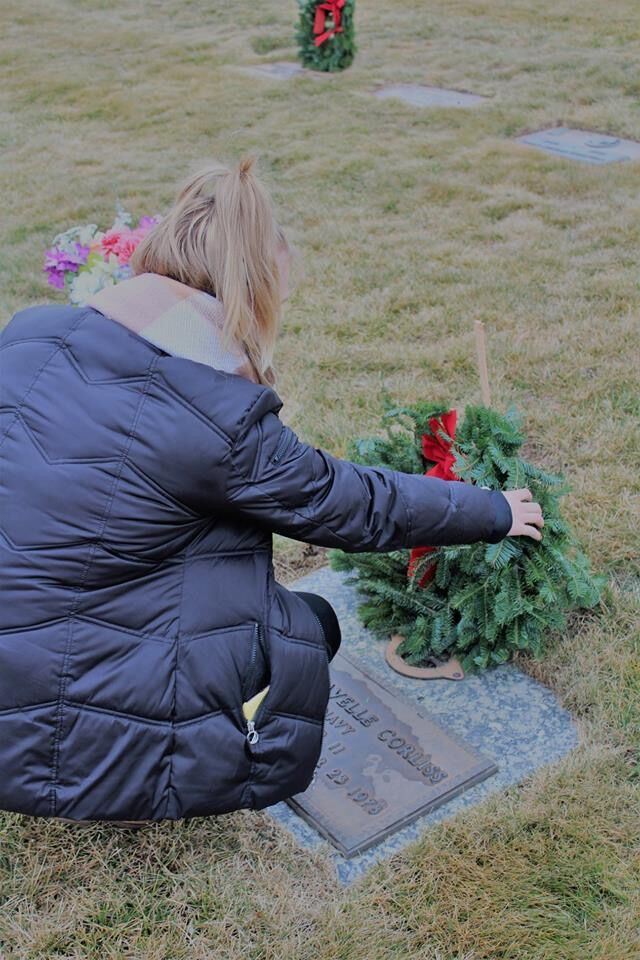 Woman paying respects by laying a wreath at a veterans grave.