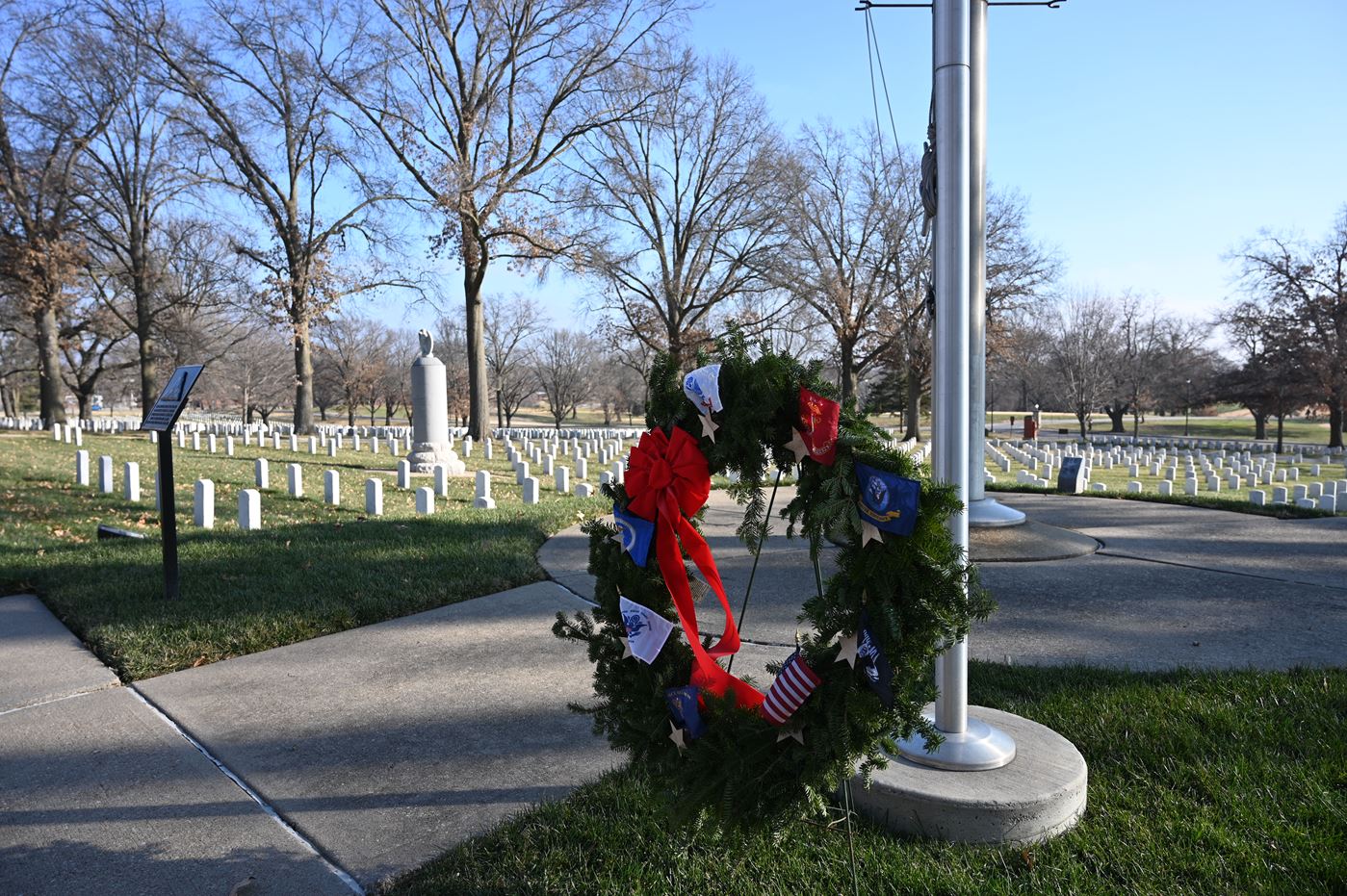 A ceremonial wreath placed at the base of the flagpole at the Fort Leavenworth National Cemetery during Wreaths Across America Day, Dec. 19, 2020. The tall monument with the eagle atop it in the background is the grave of Col. Henry Leavenworth who established "Cantonement Leavenworth" on May 8, 1827.
